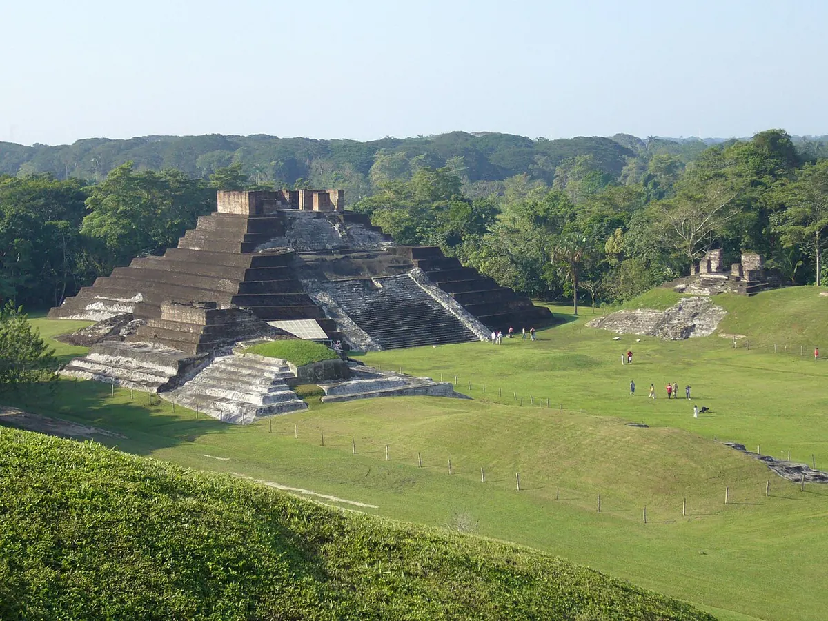 Estructuras de la zona arqueológica de Comalcalco entre pasto y árboles.