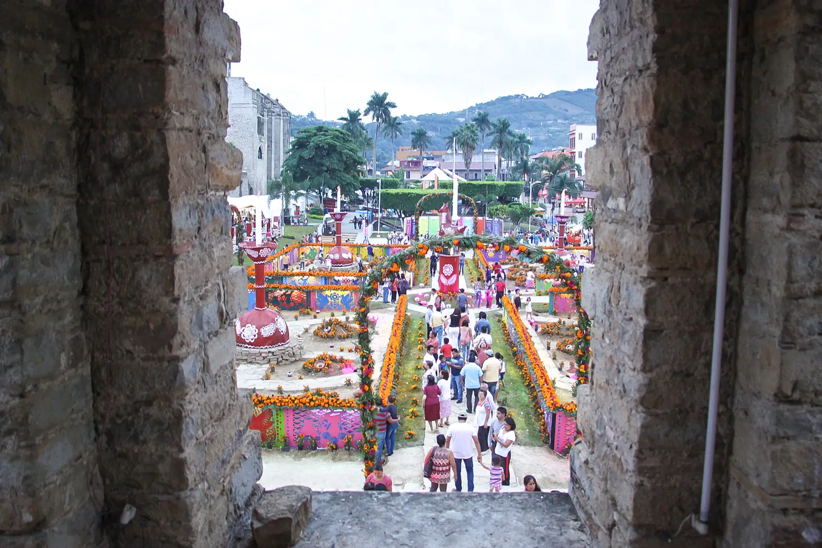 Altares y arcos de flores de cempasúchil en la plaza de Huejutla, Hidalgo, durante el Xantolo, vistos desde una ventana de piedra